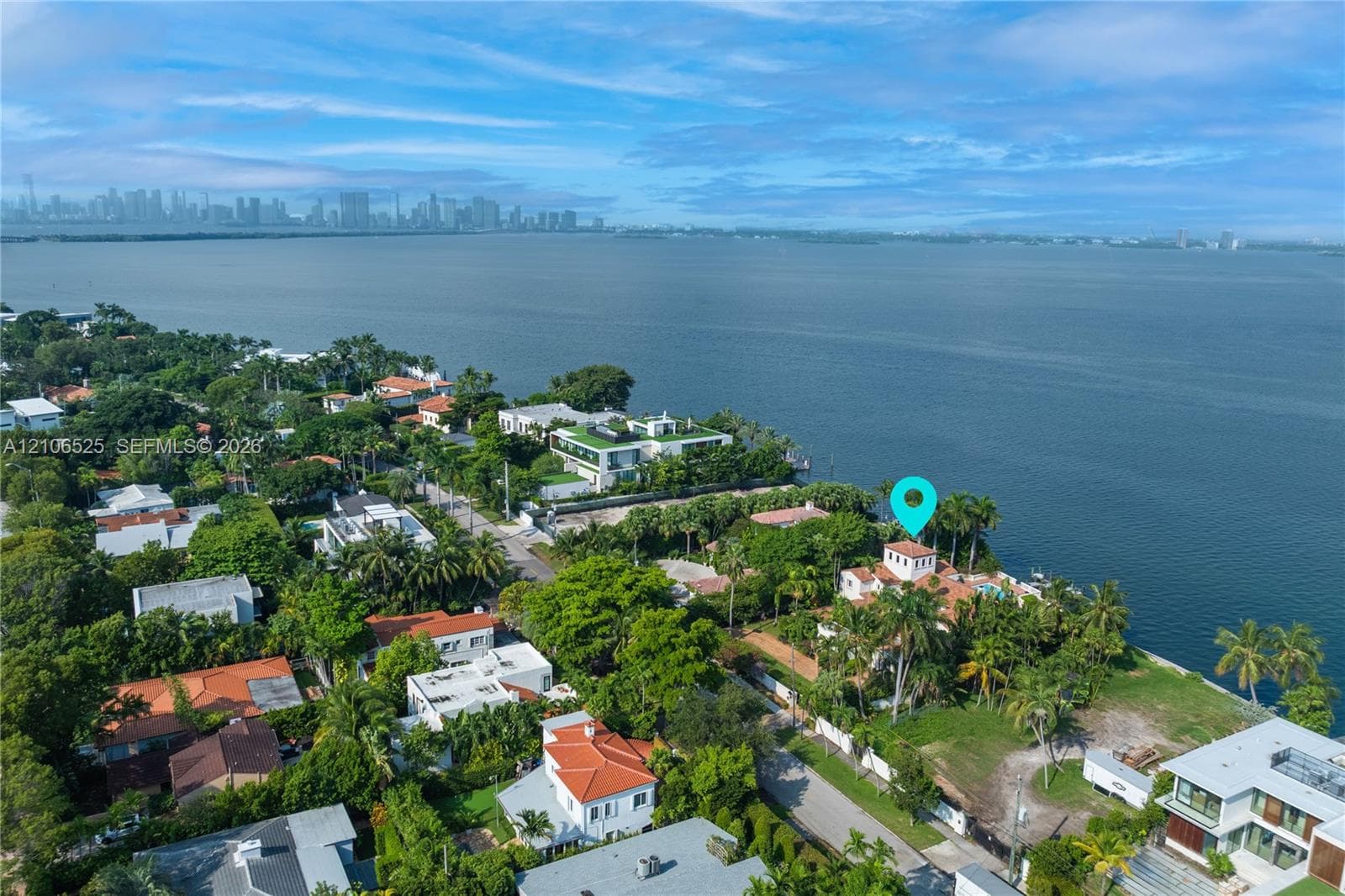 Aerial perspective of a waterfront property featuring direct water frontage, a multi-story residence with a red tile roof, and mature perimeter landscaping