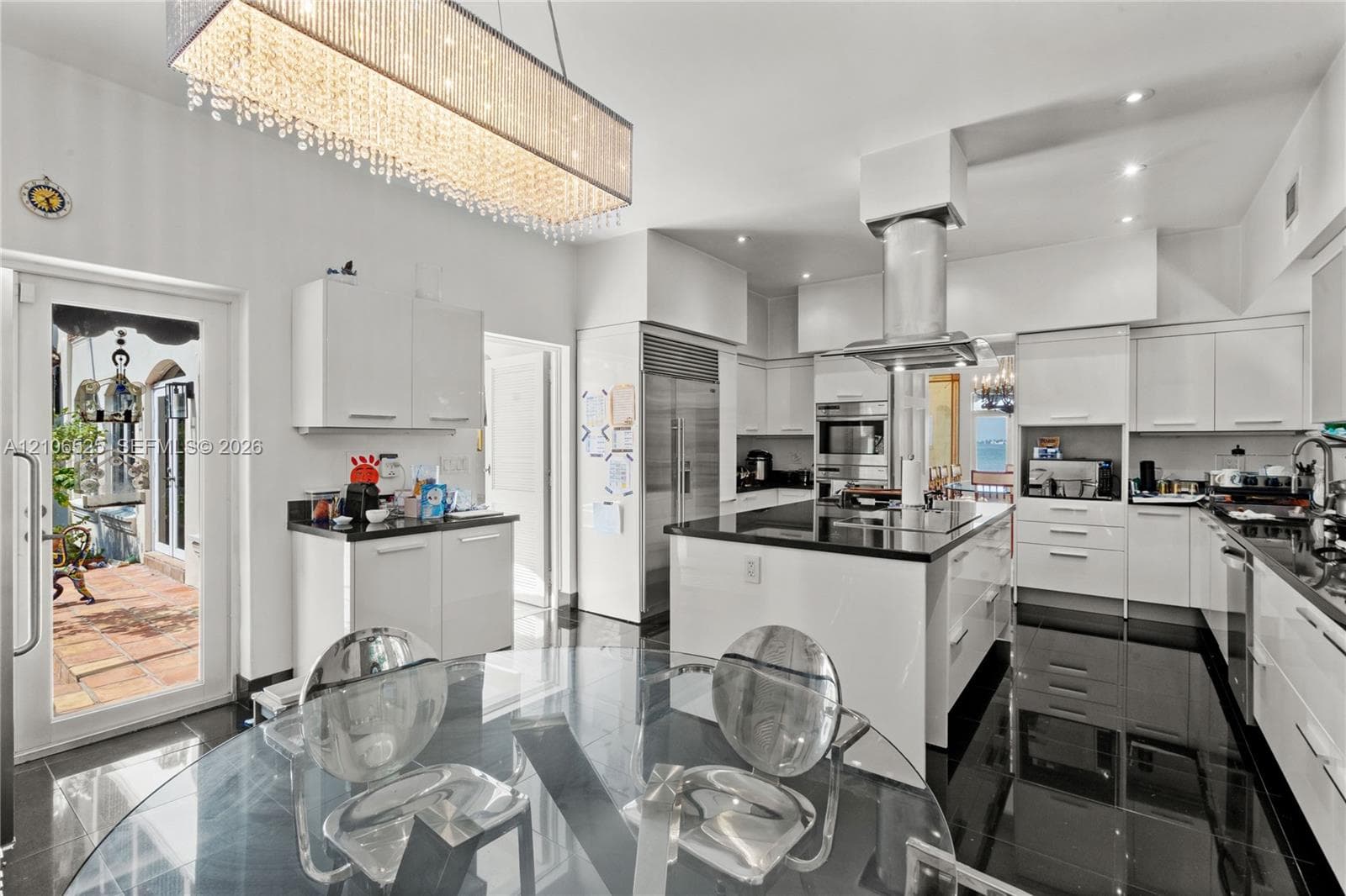 Gourmet kitchen featuring high-gloss cabinetry, a central island with a stone countertop, stainless steel appliances, a cylindrical range hood, and a linear crystal chandelier