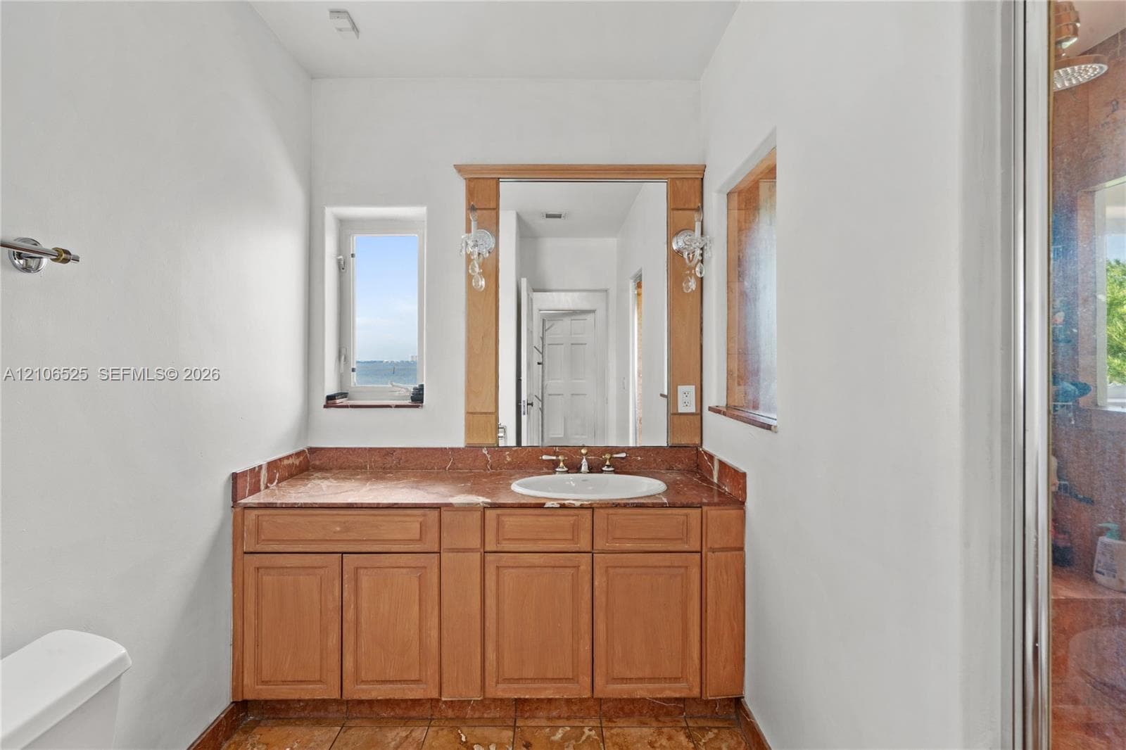Bathroom featuring a stone-topped vanity with wood cabinetry, an integrated sink, dual wall-mounted light fixtures, and stone flooring