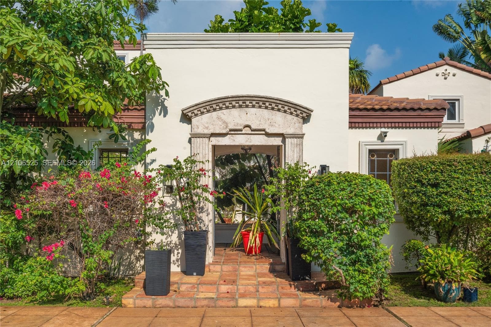 Stucco exterior featuring a decorative stone entryway arch, terra-cotta tile flooring, and terracotta roof accents