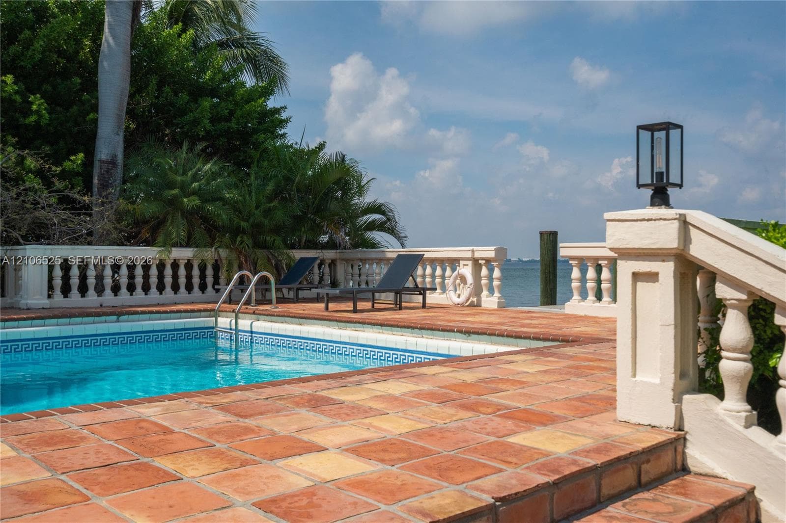 Waterfront pool terrace featuring decorative concrete balustrade railings, terracotta tile paving, and built-in lantern-style pillar lighting