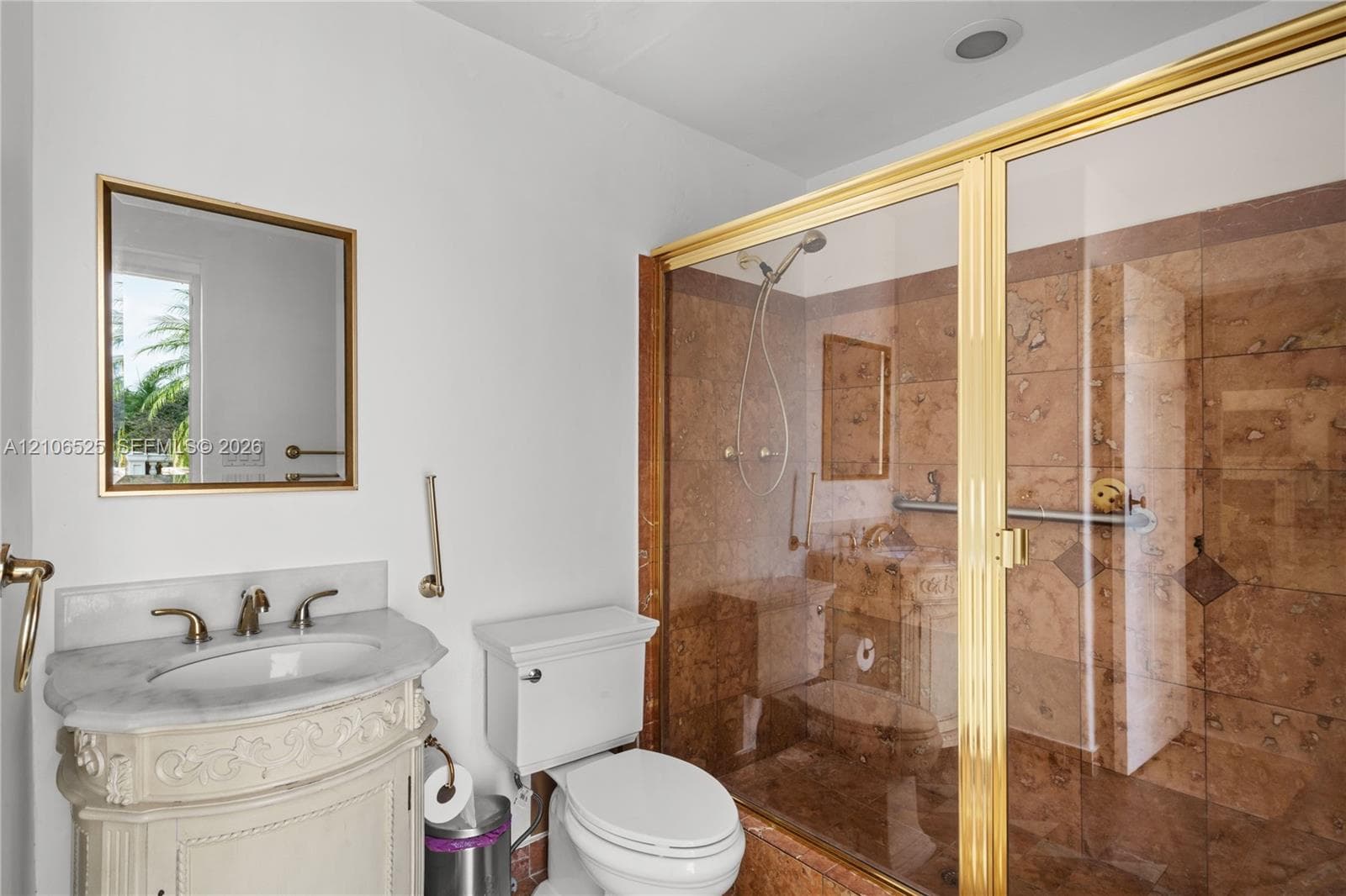 Bathroom featuring a stone-topped vanity with ornate carved base, wall-mounted mirror with gold-finish frame, and walk-in shower with floor-to-ceiling stone tile surround and gold-finish enclosure