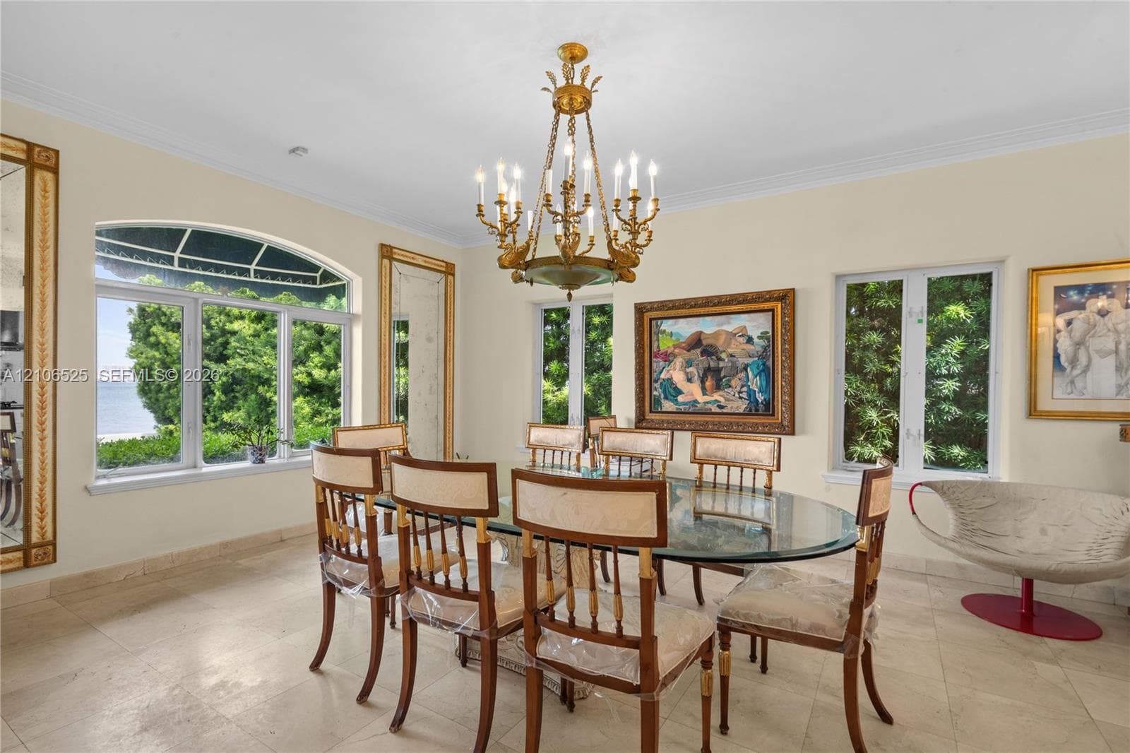Ornate brass chandelier, natural stone flooring, arched window with multi-pane glazing, and framed wall mirrors