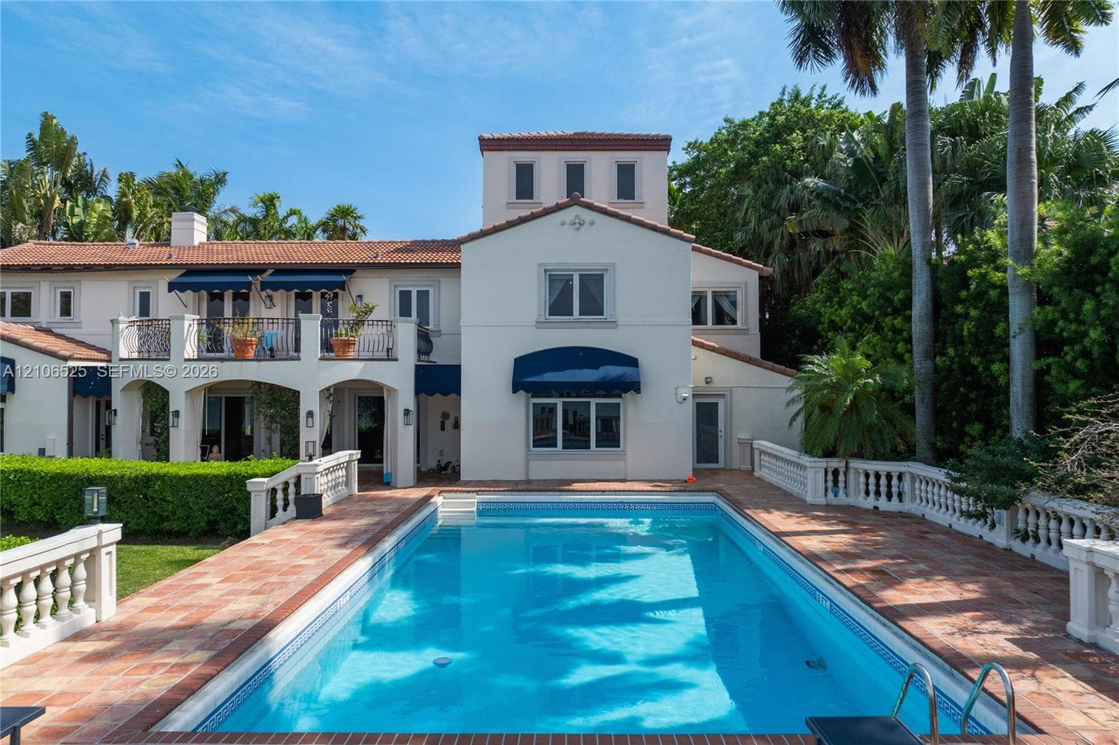Stucco exterior residence featuring a tile roof, second-story balcony, expansive pool area, and classic balustrade hardscaping