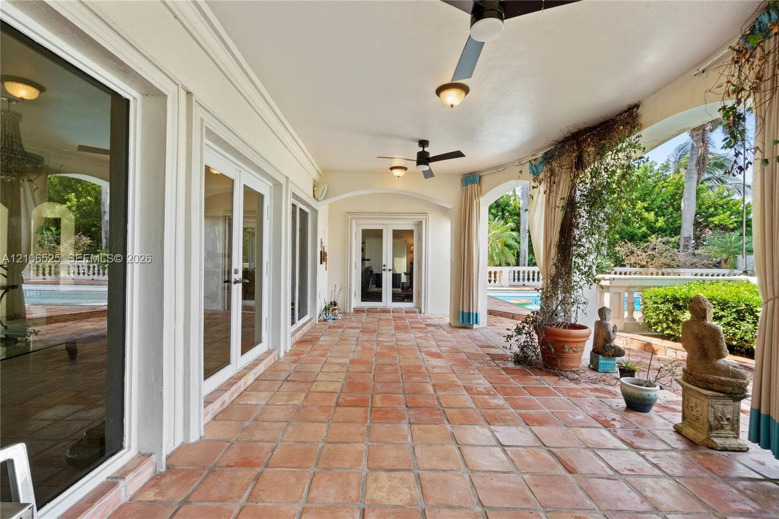 Covered terrace featuring terra cotta tile flooring, multiple sets of glass French doors, arched architectural detailing, and ceiling-mounted fans