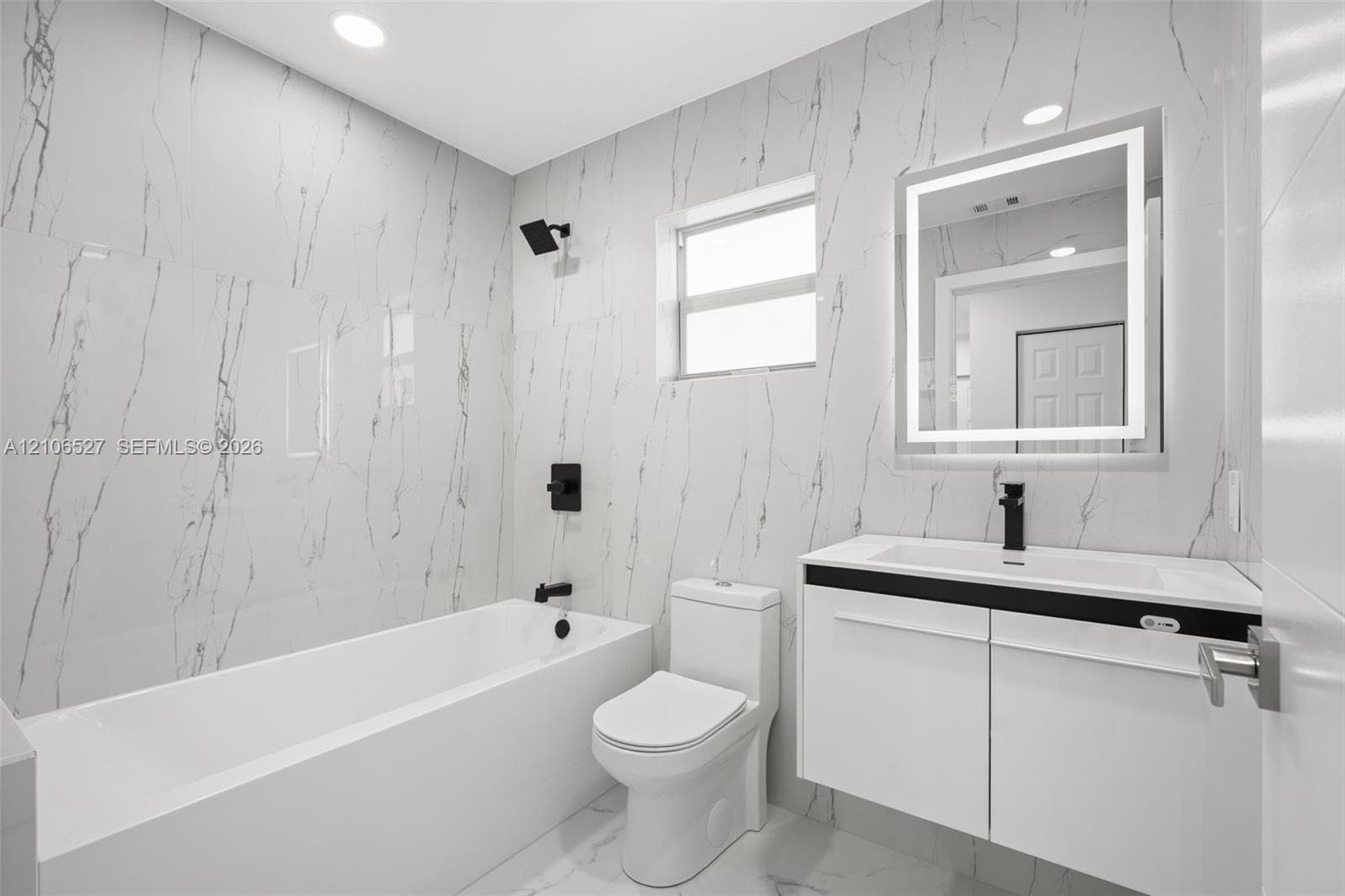 Modern bathroom featuring floor-to-ceiling large-format tile, a floating vanity with a vessel sink, a matte black faucet and shower head, and a built-in LED mirror