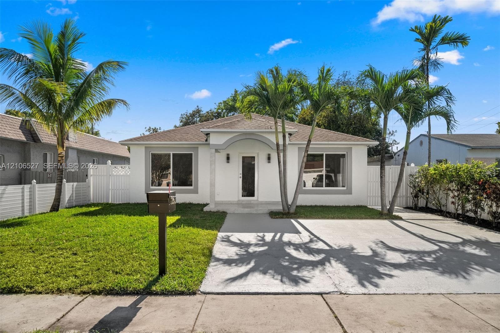 Single-story residence featuring a smooth stucco exterior, a recessed entryway with a decorative arch, a concrete driveway, and white vinyl privacy fencing