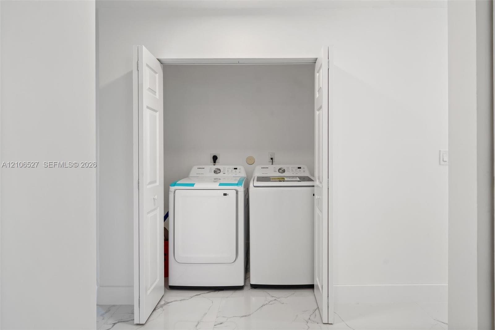 Laundry alcove featuring white bi-fold doors, white interior walls, and tile flooring