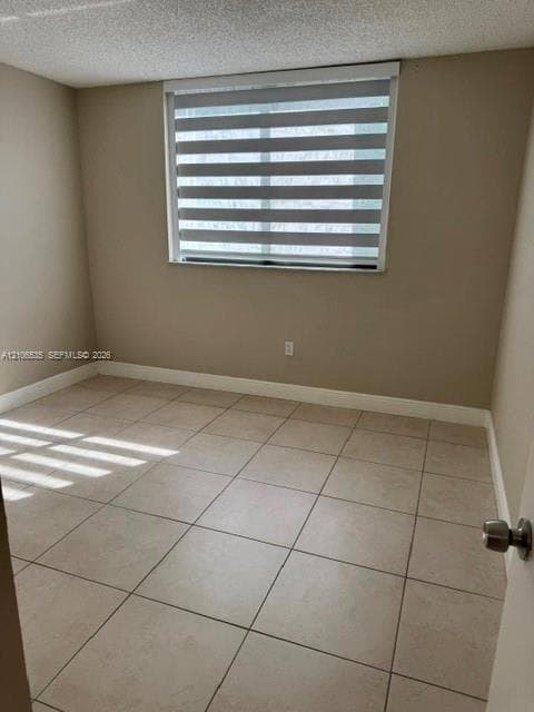 Neutral-toned interior room featuring large-format ceramic tile flooring, a textured ceiling, and a window equipped with striped horizontal roller shades