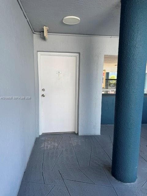 Entryway featuring a solid door, geometric patterned concrete flooring, and a structural pillar with a textured finish