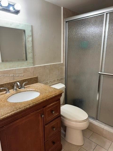 Bathroom featuring a wood vanity with a stone countertop, undermount sink, ceramic tile backsplash, and a glass-enclosed shower