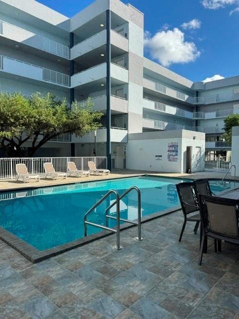Swimming pool featuring a tiled deck, metal handrails, and a white perimeter fence