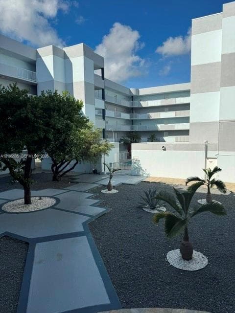 Multi-level building exterior featuring a geometric concrete walkway, xeriscaped courtyard with dark stone ground cover, and mature ornamental trees