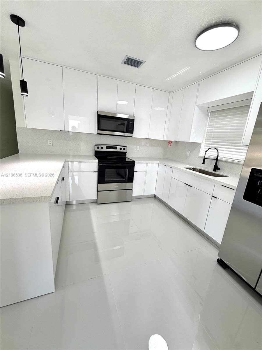 Kitchen featuring high-gloss white cabinetry, quartz countertops, large-format tile flooring, stainless steel appliances, and a matte black gooseneck faucet