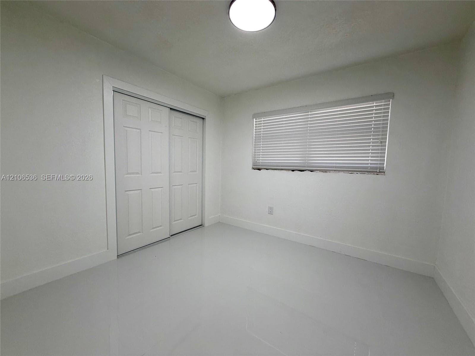 Interior room featuring polished tile flooring, white walls, a dual-panel sliding closet, and a horizontal blind-covered window