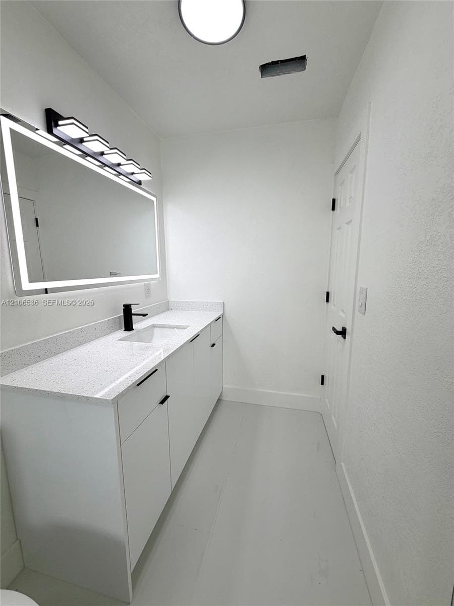 Modern vanity with a speckled countertop, integrated rectangular sink, matte black faucet, and a large backlit mirror with an integrated light fixture