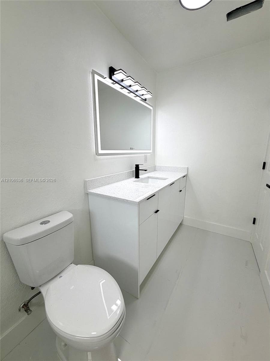 White vanity featuring a light-toned solid surface countertop, rectangular undermount sink, matte black faucet, and an integrated LED-backlit mirror