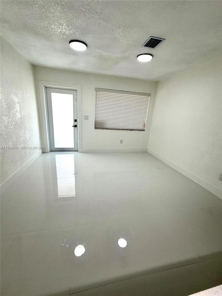 Polished large-format tile flooring, textured wall finish, dual flush-mount ceiling lighting, and a glass-paneled entry door
