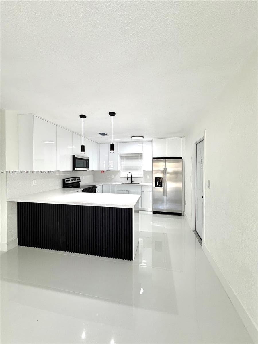 Kitchen featuring high-gloss white cabinetry, a center island with black vertical slat detailing, white stone-finish countertops, stainless steel appliances, and polished tile flooring
