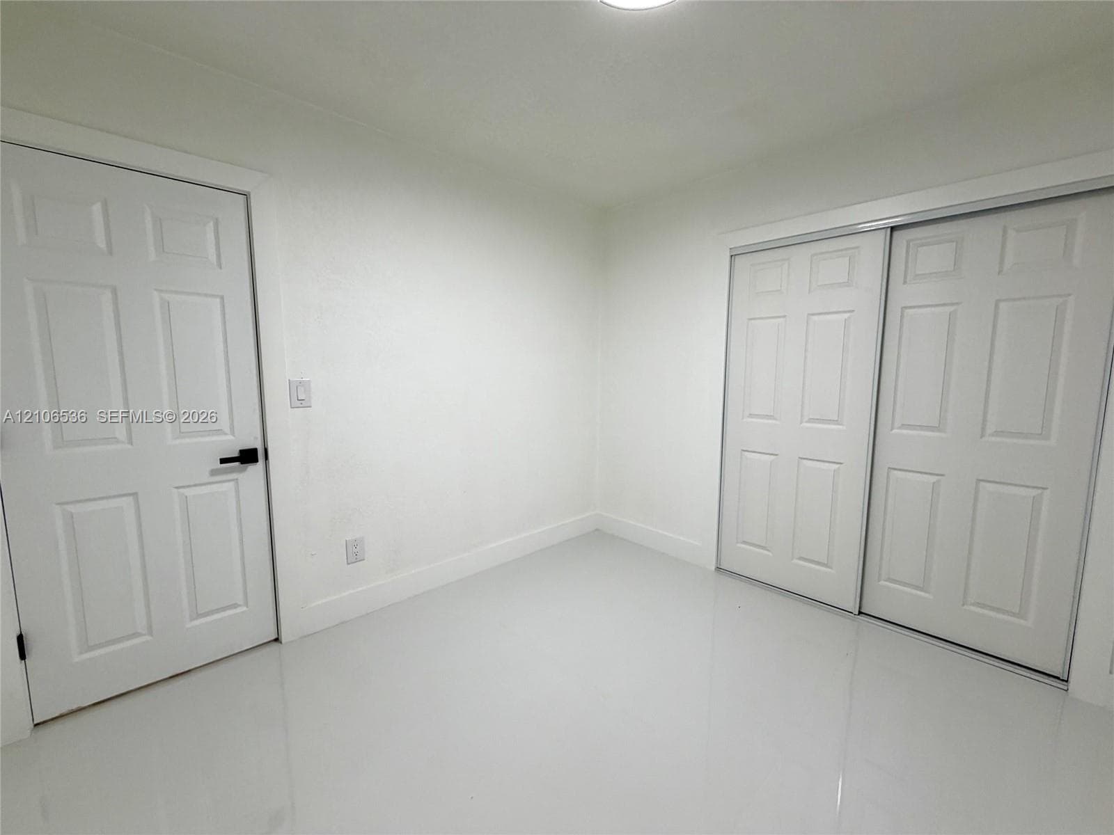 Neutral interior featuring smooth white walls, high-gloss floor tile, six-panel closet doors, and a six-panel entry door with matte black hardware