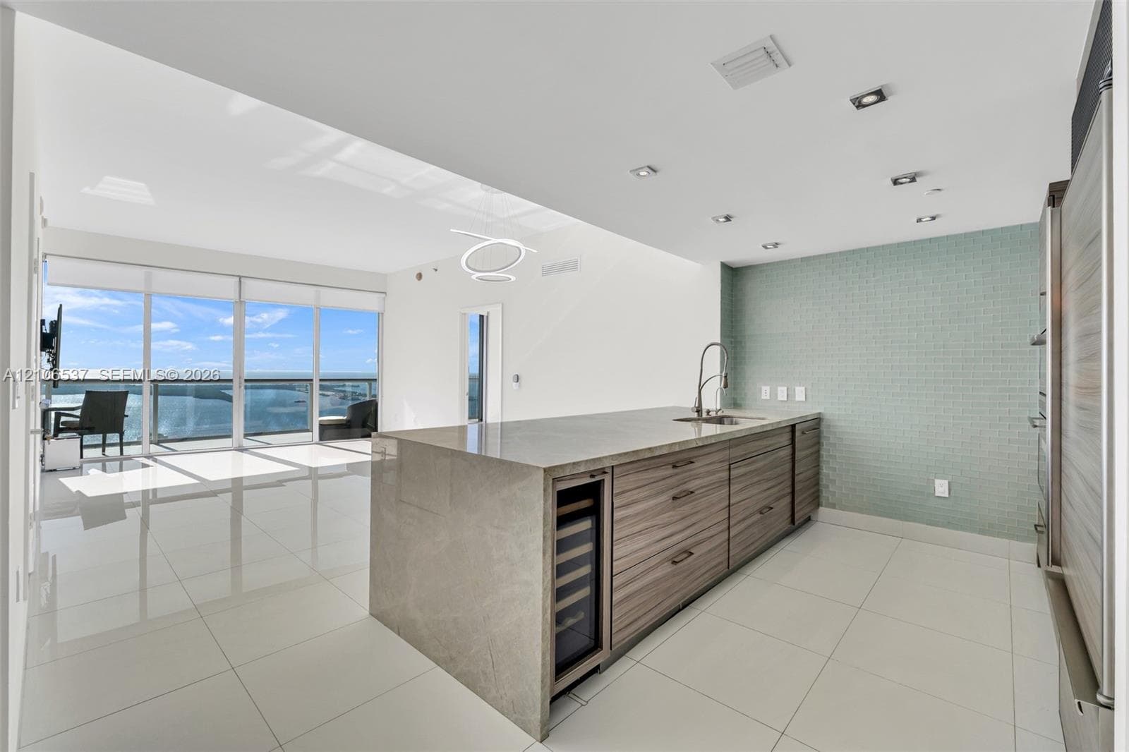 Kitchen island featuring stone countertop, wood-finish cabinetry, built-in wine refrigerator, glass tile backsplash, and floor-to-ceiling windows