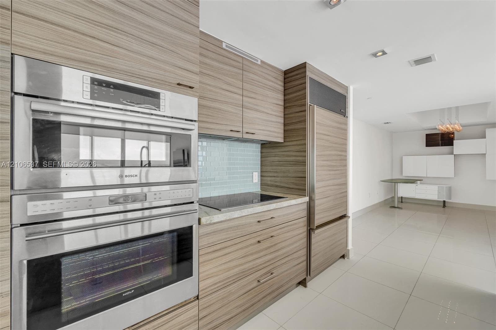 Kitchen featuring custom wood-grain cabinetry, integrated stainless steel refrigerator, Bosch wall oven and microwave, stone countertops, and tile backsplash