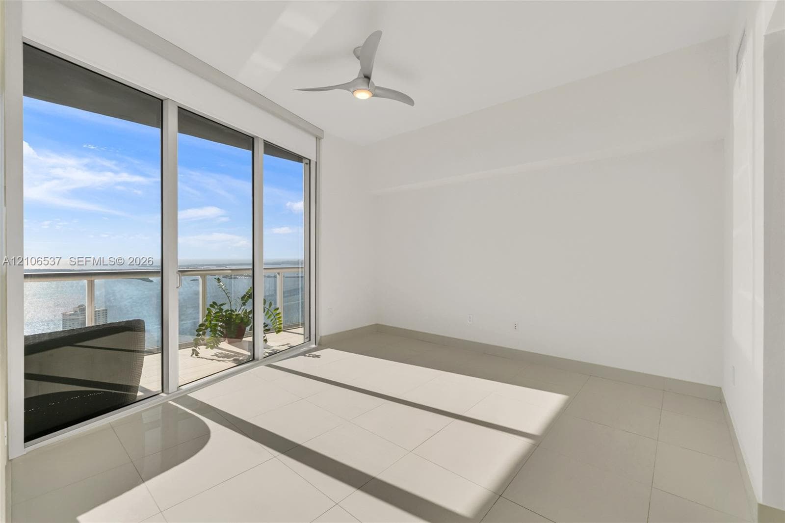 Floor-to-ceiling sliding glass doors, balcony with glass railing, large-format tile flooring, and contemporary three-blade ceiling fan