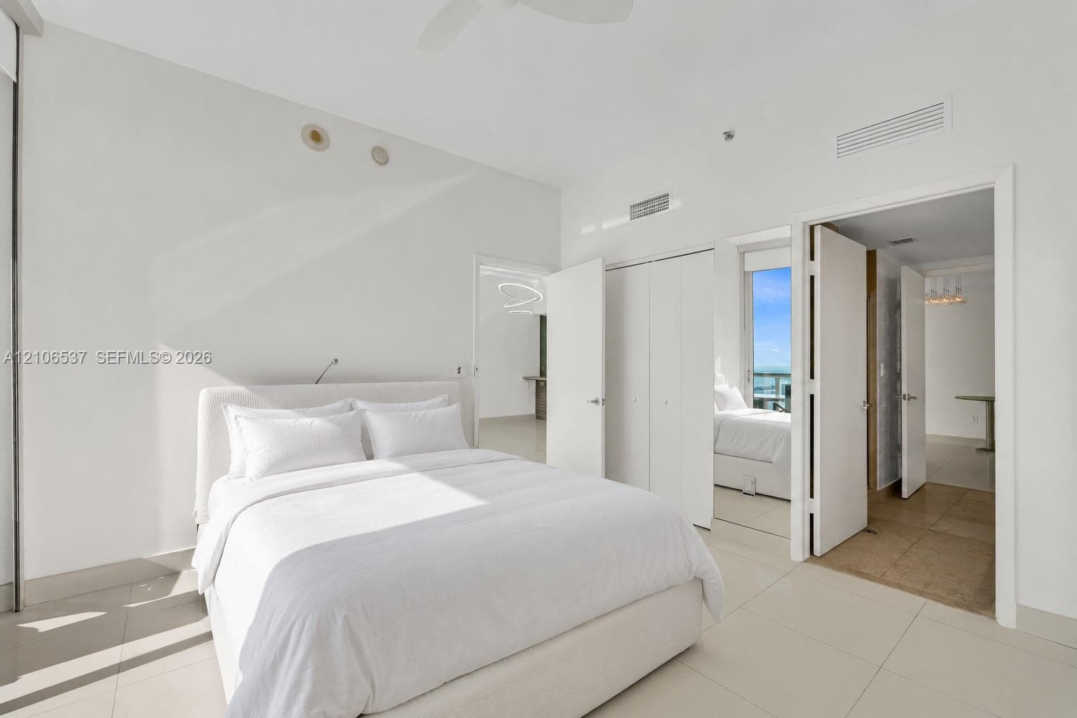 Bright room featuring large-format tile flooring, high ceilings with recessed lighting, double-door closet storage, and a private balcony with water scenery