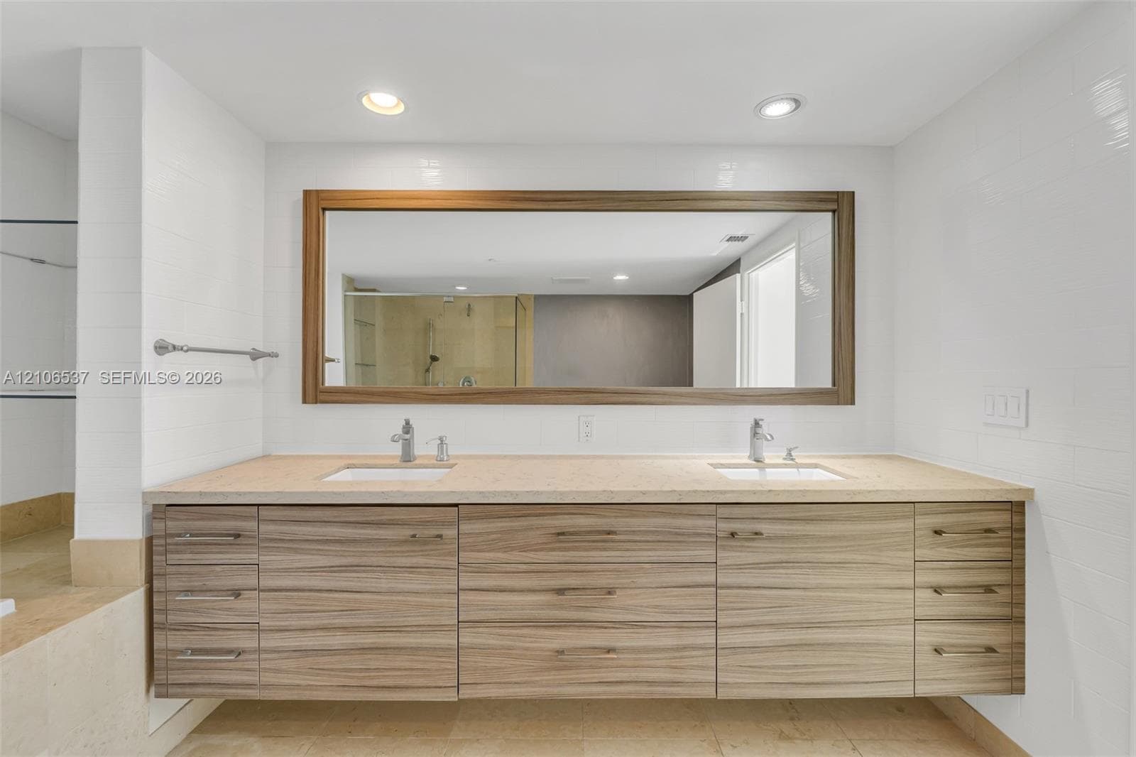 Floating vanity featuring wood-grain cabinetry, dual undermount sinks, stone-surface countertop, and a large framed mirror with integrated recessed lighting
