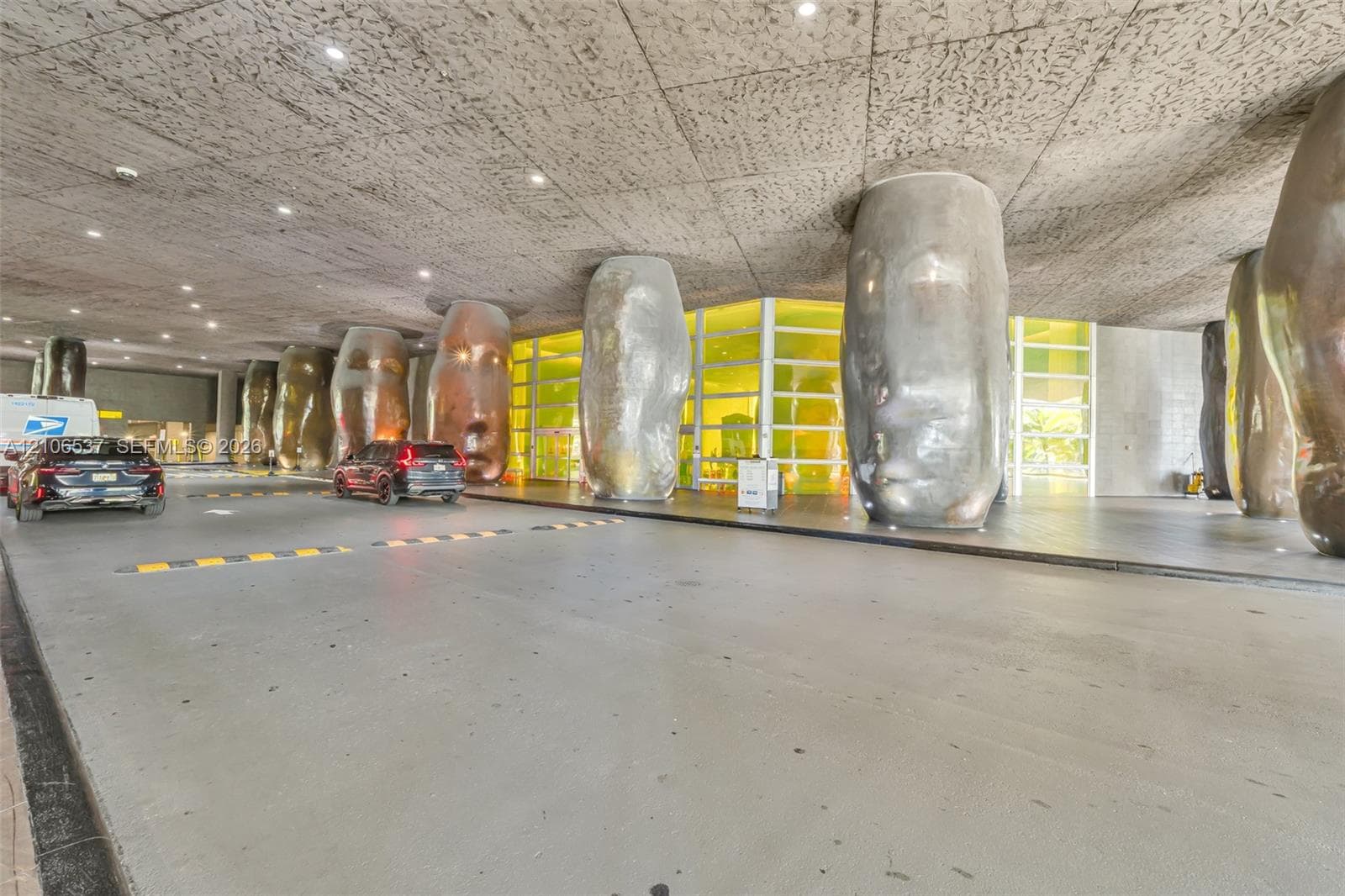 Covered porte-cochère featuring a textured concrete ceiling, recessed lighting, and sculptural metallic columns