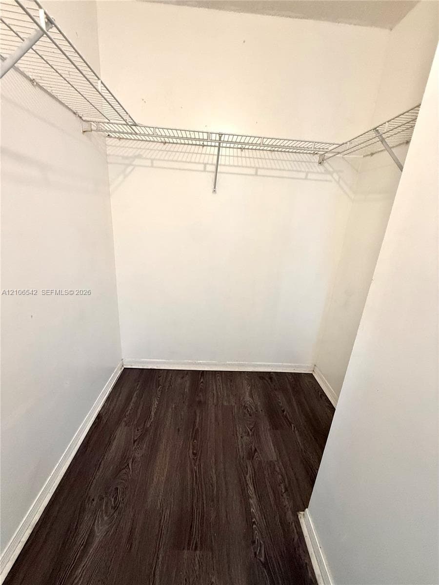 Walk-in storage space featuring dark wood-finish flooring and dual-tier wire shelving