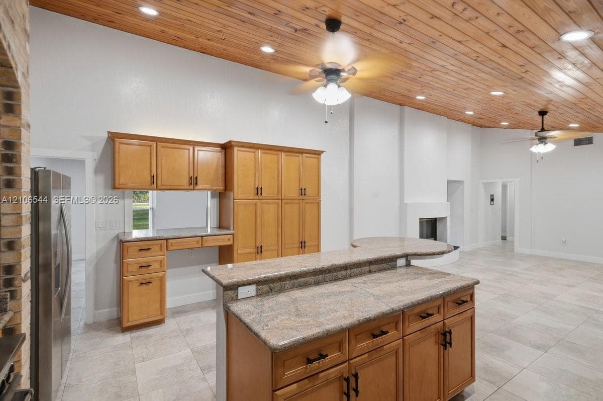 Vaulted wood-plank ceiling, stone-surfaced kitchen island with breakfast bar, built-in cabinetry, ceramic tile flooring, and integrated fireplace