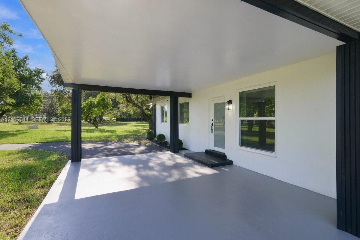 Covered entryway featuring a concrete floor, dark structural columns, a frosted glass entry door, and an exterior wall light fixture