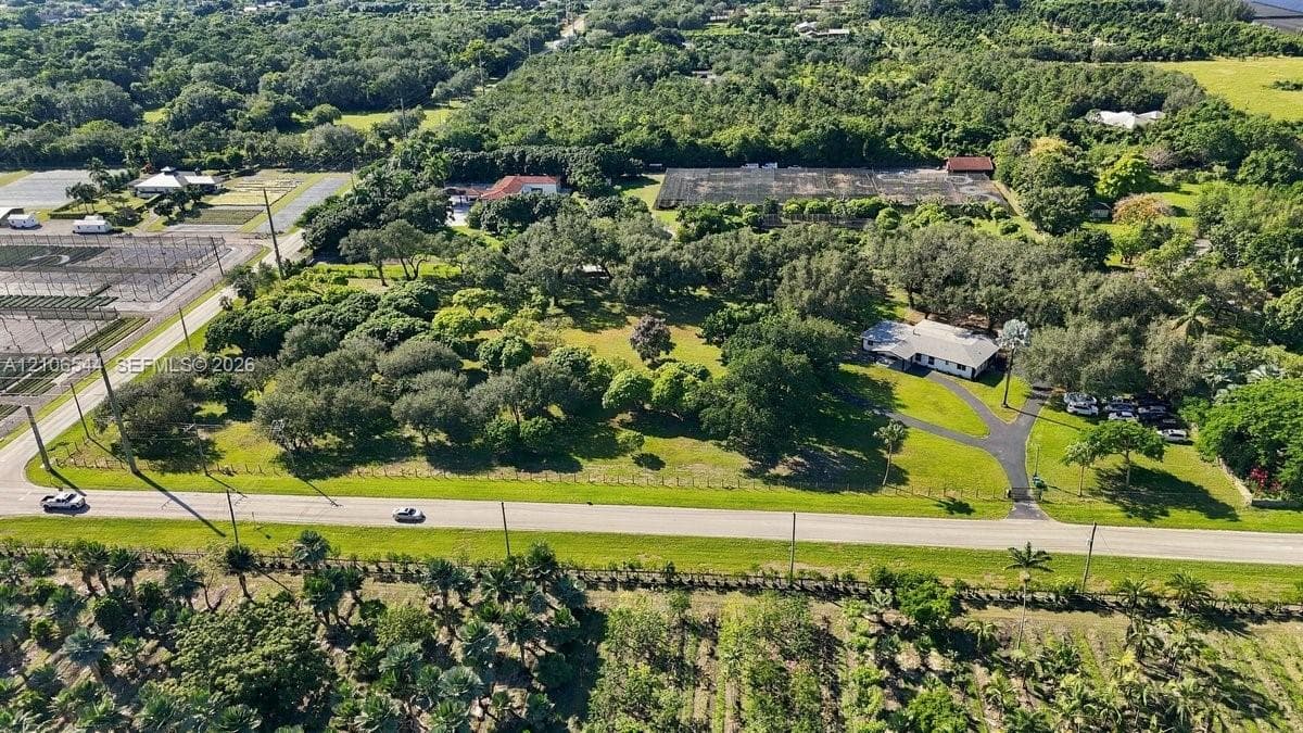 Aerial perspective of a sprawling property featuring mature canopy trees, an expansive lawn, a paved circular driveway, and perimeter fencing