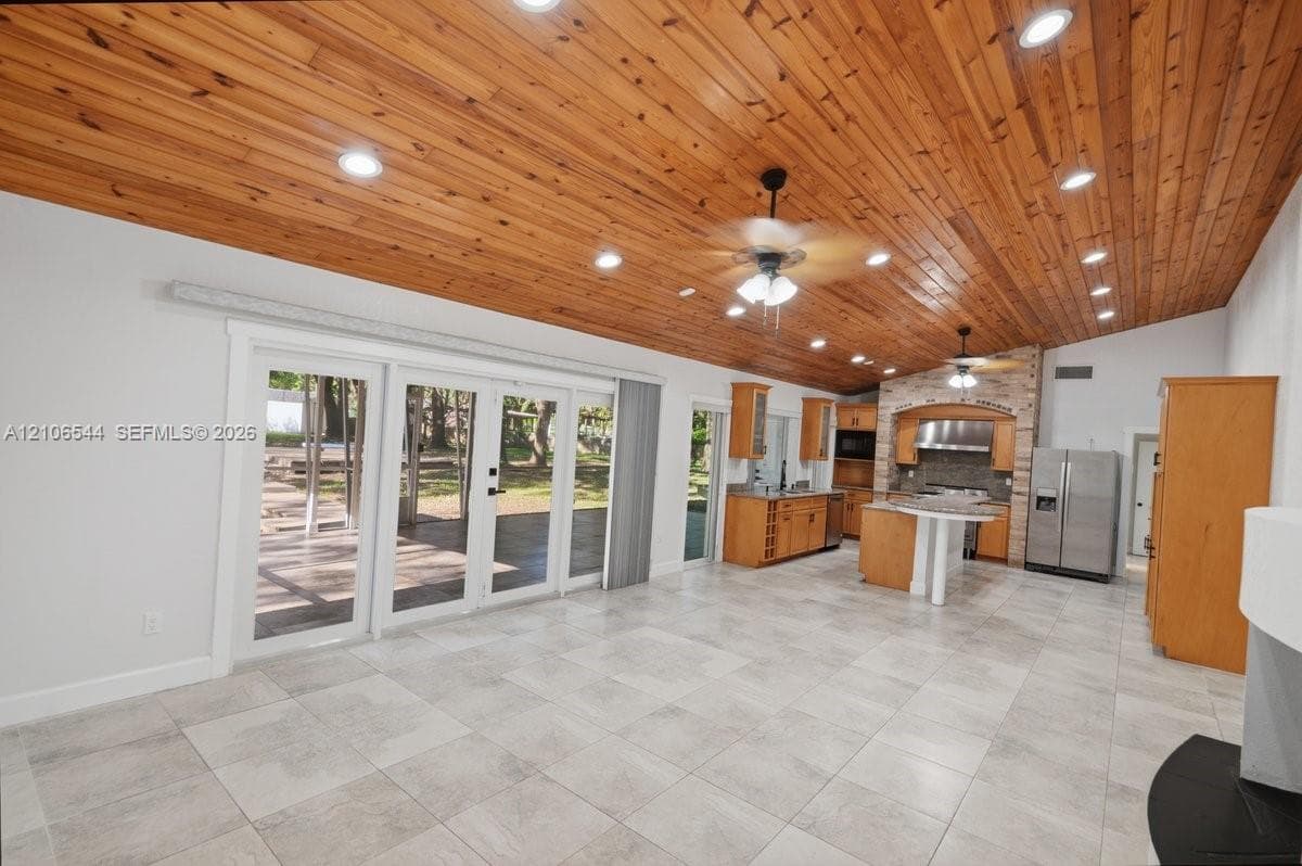 Vaulted wood-plank ceiling, neutral tile flooring, recessed lighting, double glass-panel doors, and built-in cabinetry with stone-finish countertops