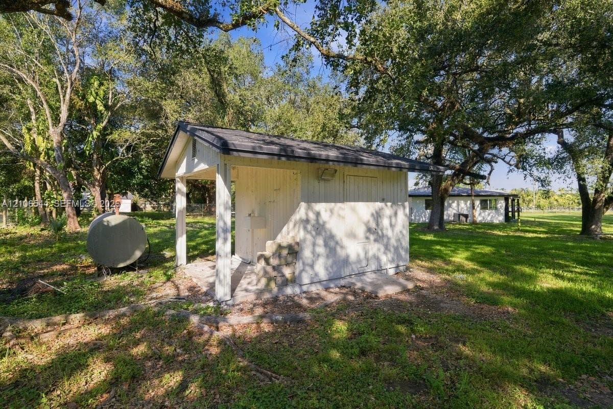 Outbuilding with white vertical siding, pitched roof, and concrete pad situated on an expansive lot with mature trees