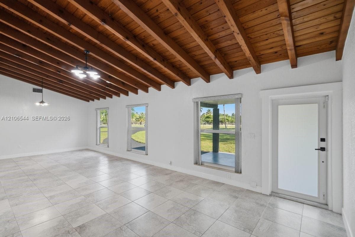 Vaulted ceiling with exposed wood beams, light-toned stone-finish flooring, and multiple windows