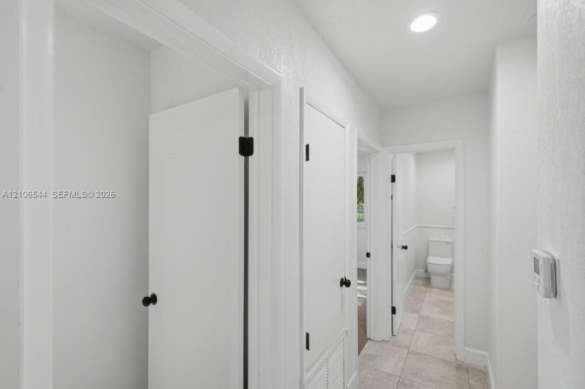 Hallway featuring neutral-toned tile flooring, recessed ceiling lighting, crisp white walls, and matte black door hardware