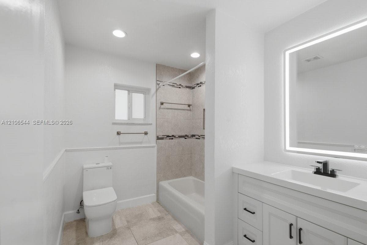 Bathroom featuring a vanity with quartz countertop, an integrated LED-backlit mirror, tile flooring, and a shower-tub combination with decorative tile inlay
