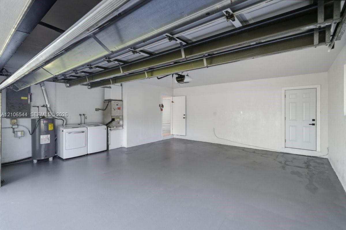 Garage interior featuring painted flooring, overhead door mechanism, integrated water heater, and a dedicated utility area with built-in laundry hookups