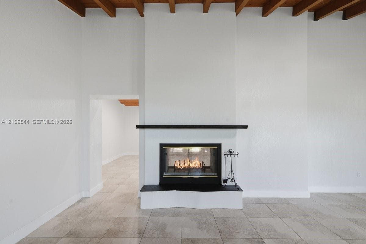Fireplace featuring a black hearth, mantle, and glass-enclosed insert, set against a floor-to-ceiling surround with exposed wood ceiling beams and large-format tile flooring