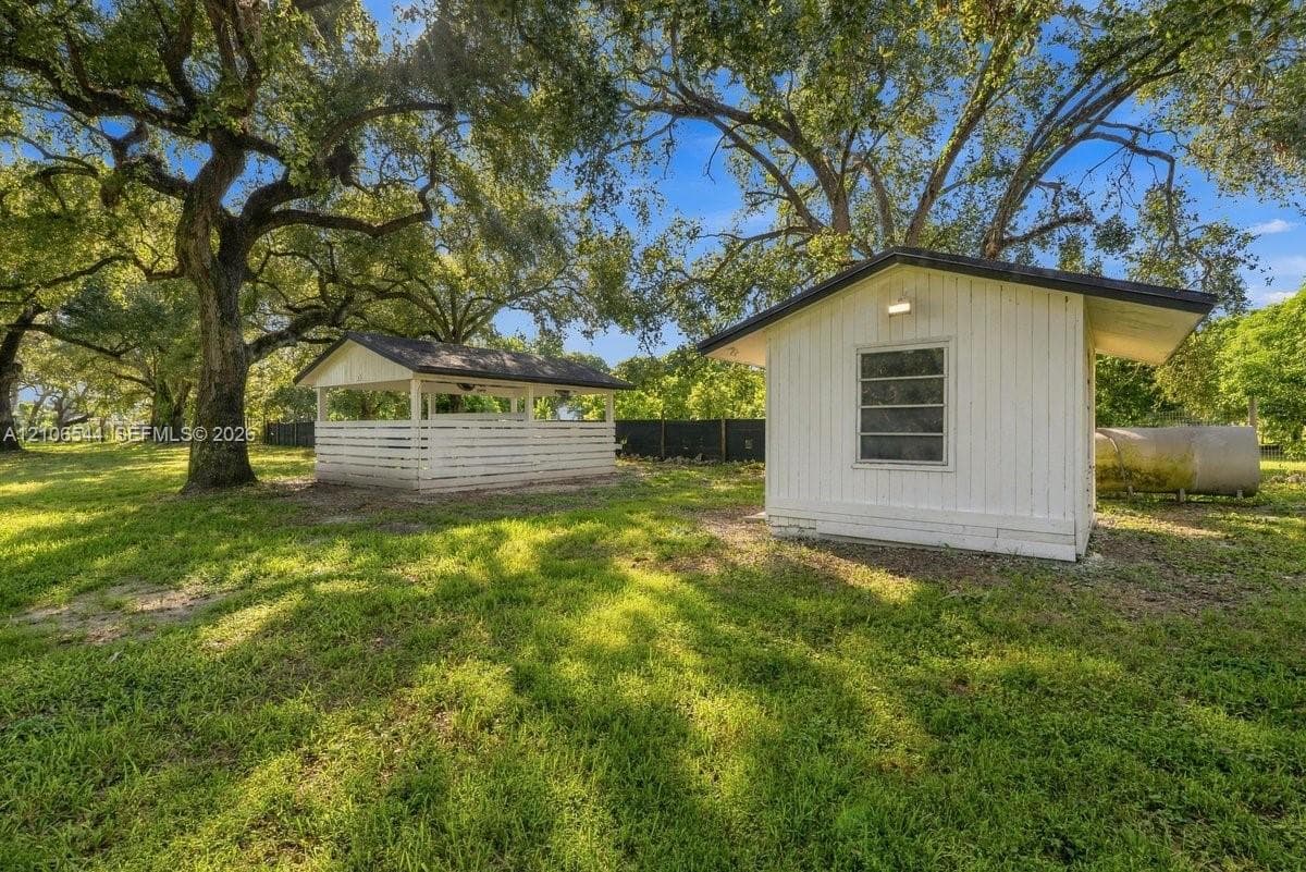 Expansive outdoor grounds featuring white-painted outbuildings, a horizontal-slat enclosure, mature canopy trees, and lawn