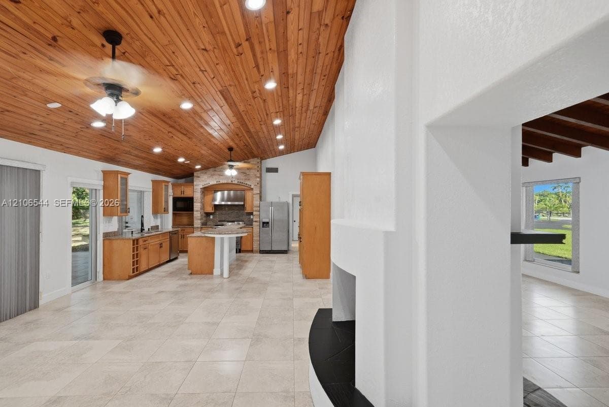 Vaulted wood-plank ceiling featuring recessed lighting, tile flooring, built-in cabinetry, center island with stone surfacing, and stone-accented fireplace surround