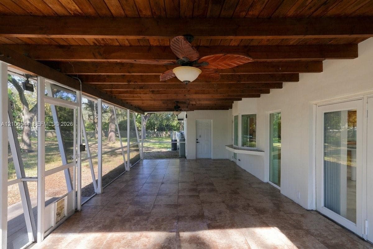 Screened-in patio featuring an exposed timber beam ceiling, tile flooring, built-in wall shelf, and ceiling-mounted fans