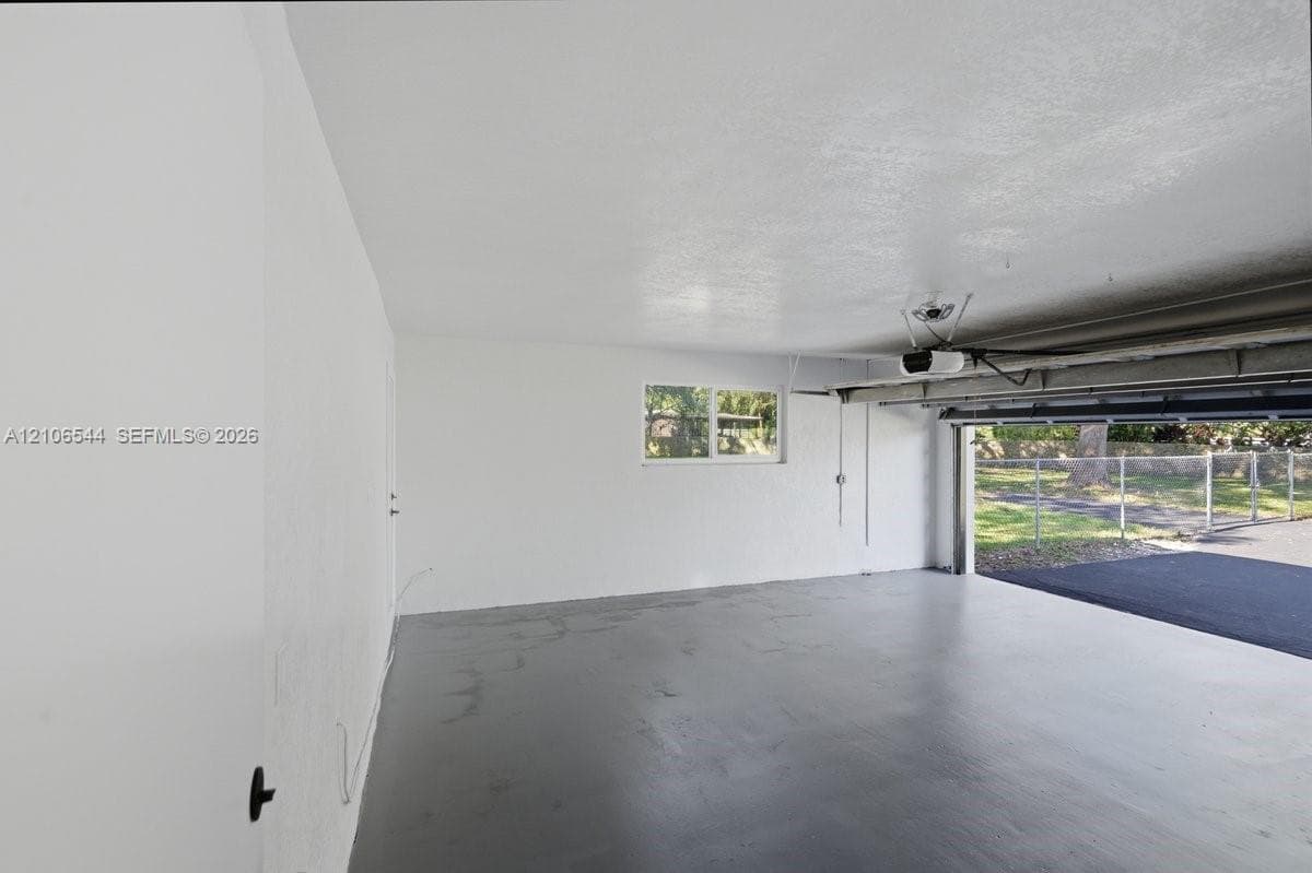 Two-car garage featuring painted concrete flooring, smooth interior walls, an installed ceiling-mounted garage door opener, and a single-pane window