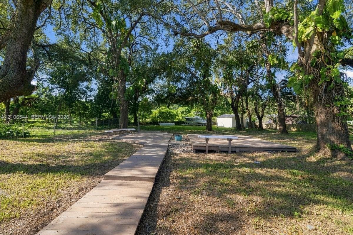 Expansive lot featuring a wood-plank walkway, raised timber platform, integrated benches, mature canopy trees, and stone ground cover