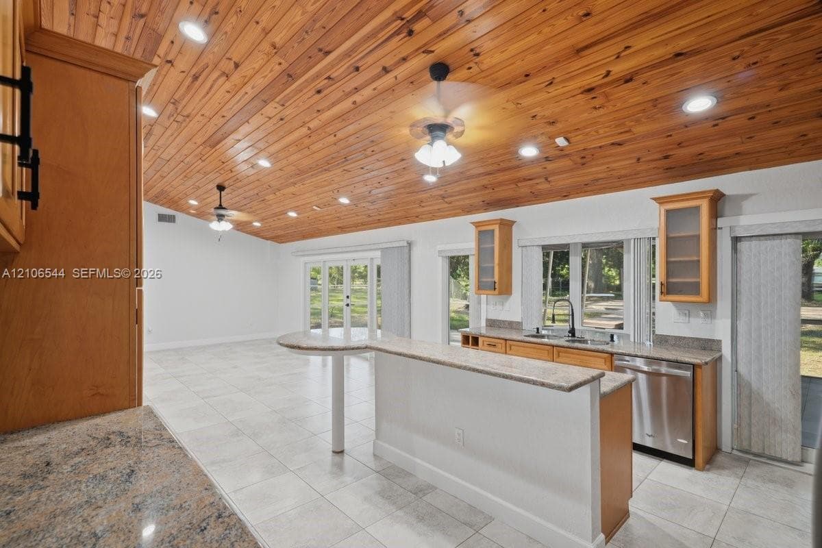 Vaulted wood-plank ceiling featuring recessed lighting and dual ceiling fans, tile flooring, stone-surfaced countertops, and stainless steel dishwasher