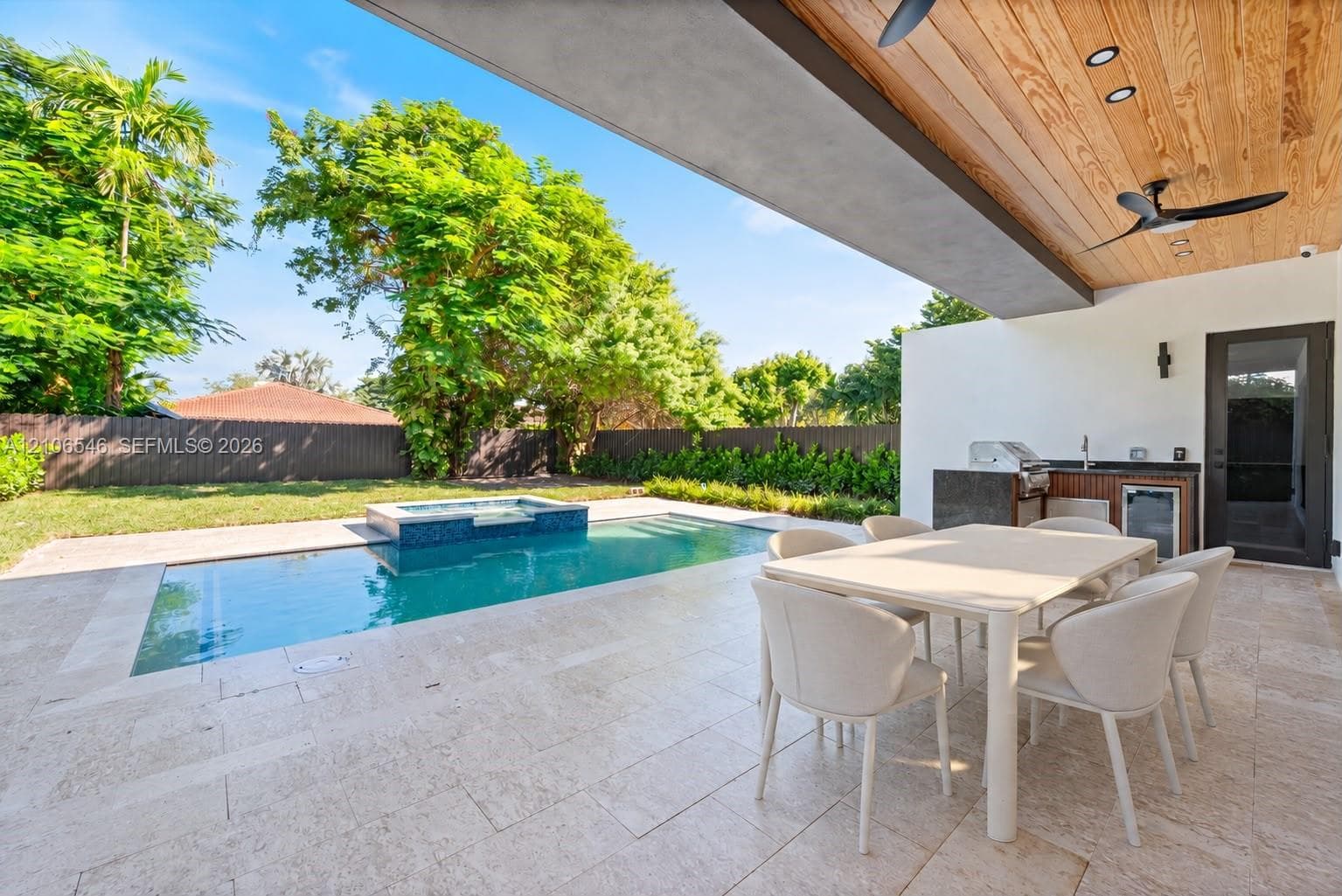 Covered outdoor patio featuring a wood-plank ceiling, natural stone pavers, built-in summer kitchen with an integrated grill, and a pool with an attached spa