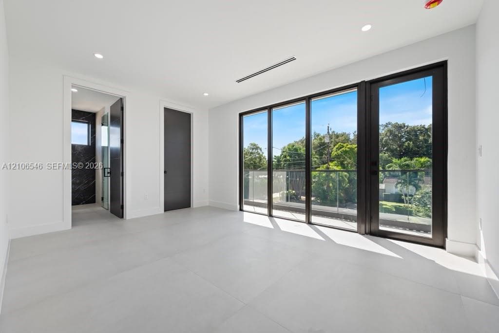 Interior space featuring large-format tile flooring, recessed ceiling lighting, full-height glass doors with dark frames, and a glass-railing exterior balcony