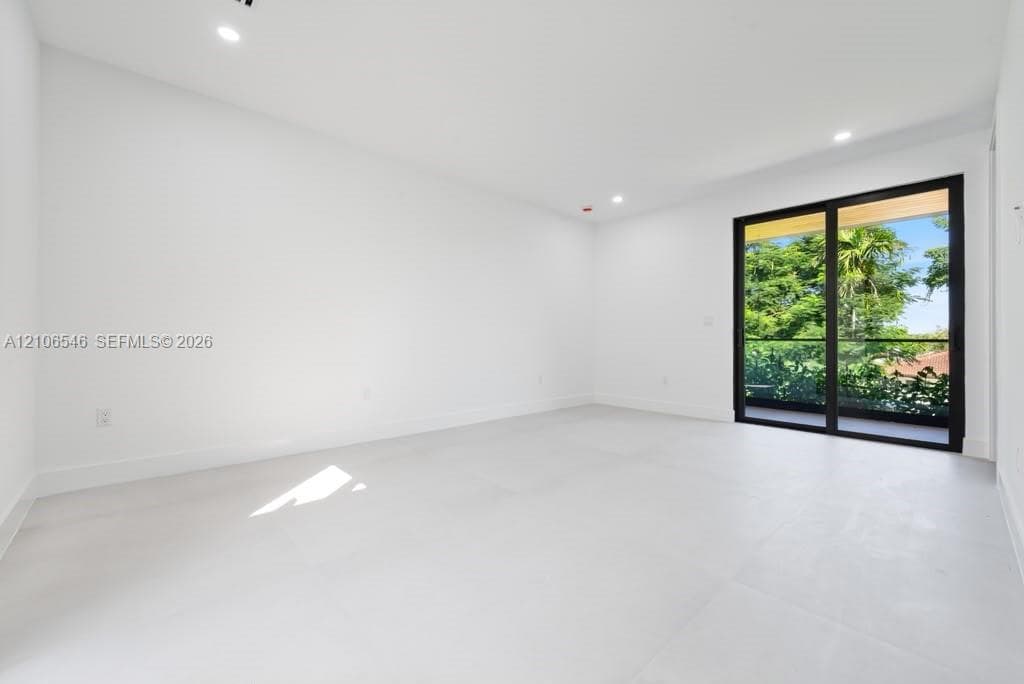 Interior space featuring large-format light-toned tile flooring, recessed ceiling lighting, and black-framed sliding glass doors opening to an exterior balcony